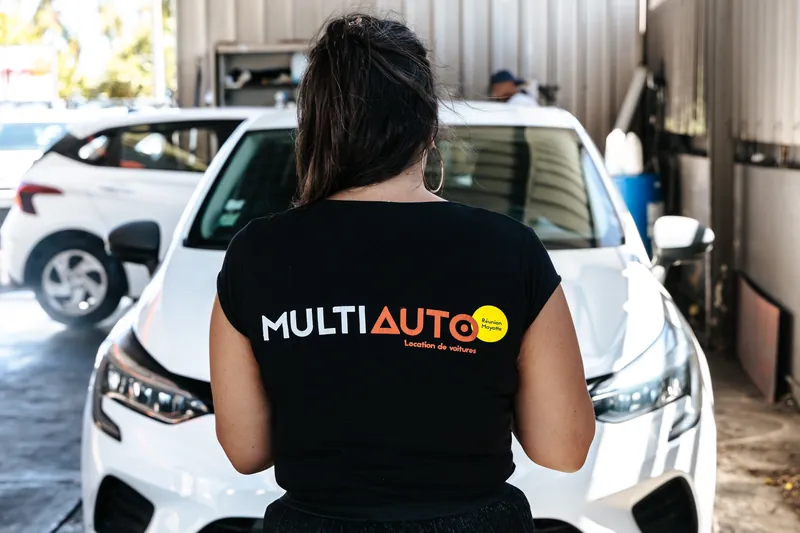 Membre de l’équipe MultiAuto en t-shirt de l’agence, devant une voiture de location à La Réunion