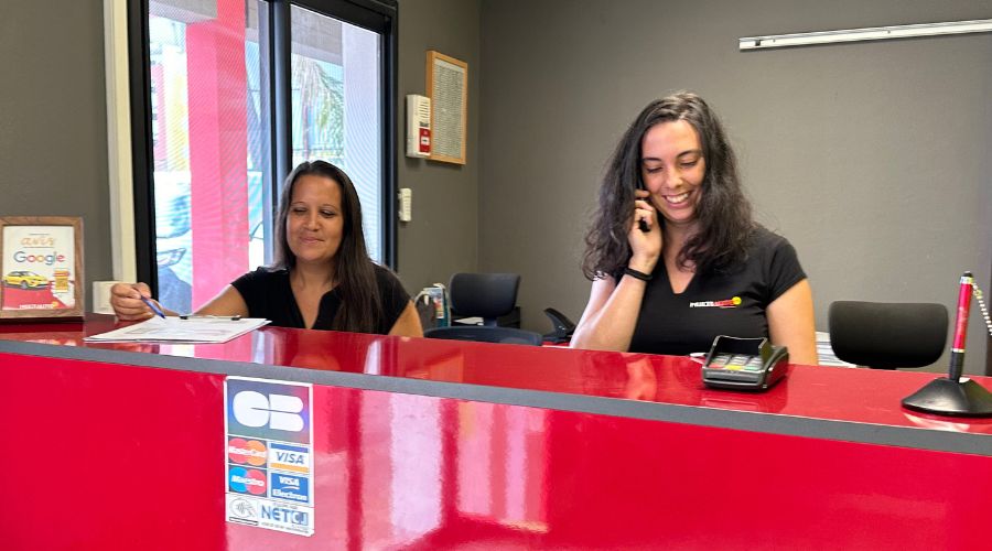 Deux hotesses d'accueil souriantes et professionnels de la location voiture se tenant derrière un comptoir, prêts à vous accueillir.