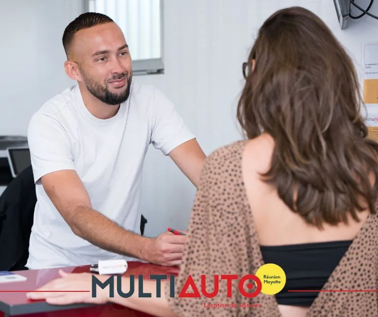 Conseiller Multi Auto en discussion avec une cliente au comptoir d'une agence de location de voitures à La Réunion.